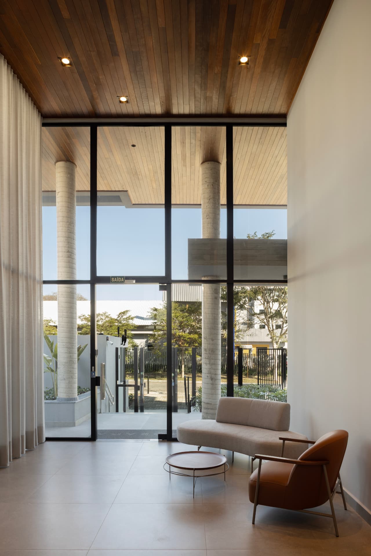 Hall de entrada do Ed. Morada com pé-direito duplo, concreto e madeira